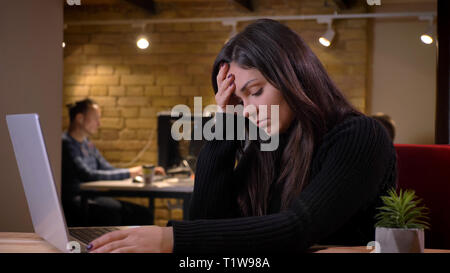 Portrait of middle-aged overweight businesswoman working with laptop and thinking on office background. Stock Photo