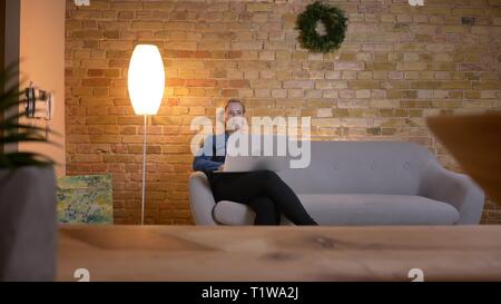 Portrait in profile of senior caucasian woman sitting on sofa in front of laptop and thinking about something in cozy home atmosphere. Stock Photo