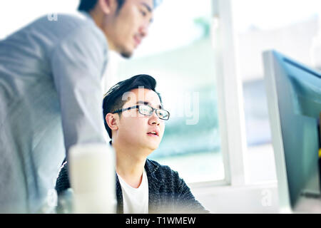 two young asian businessmen having a discussion in front of desktop computer in office. Stock Photo