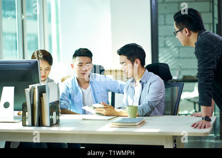 four young asian corporate executives working together discussing business plan in office. Stock Photo
