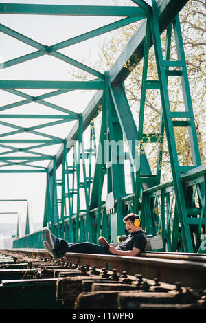Young construction worker man rests sitting reading a book on an old steel railway bridge Stock Photo