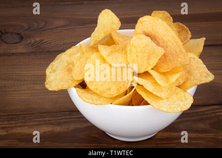 Crispy potato chips in bowl on wooden background. Stock Photo