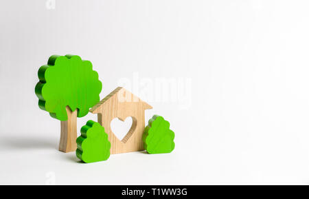 A house with a heart and wooden figures of trees with bushes. The concept of a love nest. Acquisition of affordable housing in a mortgage or loan. Acc Stock Photo