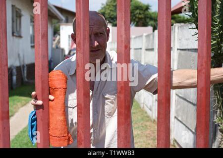 Middle aged Afrikaner man looks out from behind his security gate in Johannesburg Stock Photo