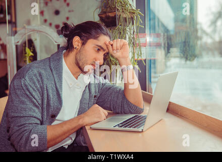 Frustrated businessman sitting on desk with hand on head looking worried at laptop. Portrait of a handsome guy wearing formal  clothing sitting near w Stock Photo