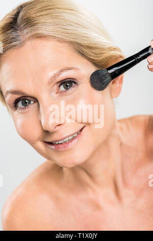 beautiful and smiling woman applying blush with cosmetic brush and looking at camera Stock Photo