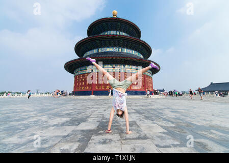 Beijing, China - 08 01 2016: A girl making a handstand with legs apart in font of the Temple of Heaven in Beijing, China. A wonderful historic chinese Stock Photo