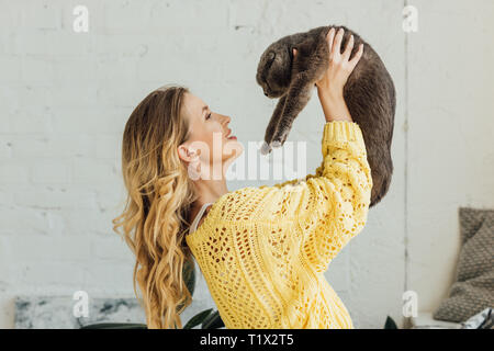 side view of beautiful girl in knitted sweater holding scottish fold cat at home Stock Photo