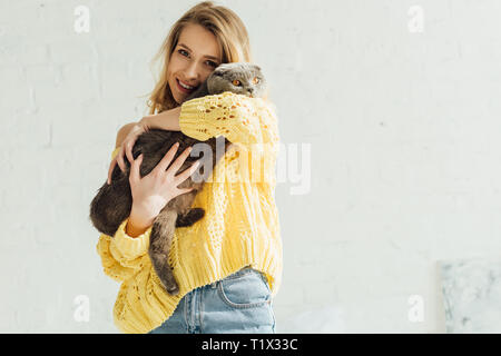 beautiful smiling girl in knitted sweater looking at camera and embracing scottish fold cat Stock Photo