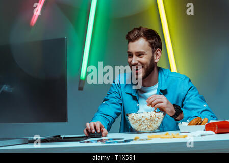 handsome and smiling man holding computer mouse and eating popcorn Stock Photo