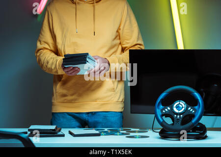 cropped view of man standing and holding compact disks with video games Stock Photo