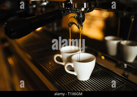 The moment of the brewing process of espresso. Coffee pours into two white cups. Stock Photo