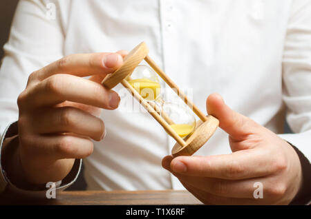 Hourglass in the hands of a businessman in a white shirt. Planning time and reducing business costs. Catch all and do all planned things. Time saving. Stock Photo