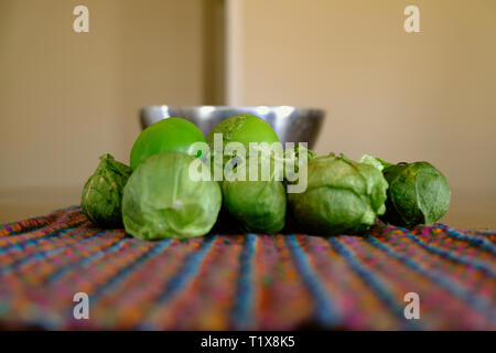 A pile of green tomatillos (Physalis philadelphica) on a colorfully patterned fabric; tomatillos with husks; peeled tomatillos. Stock Photo
