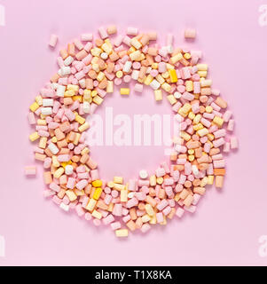 Top view of the multi-colored marshmallows which lies in the shape of a round frame with an area for text in the center on a monochrome pink backgroun Stock Photo