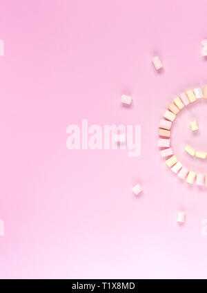 Top view of the multi-colored marshmallows which lies in the shape of a smiley or sun on a one-color pink background. Stock Photo