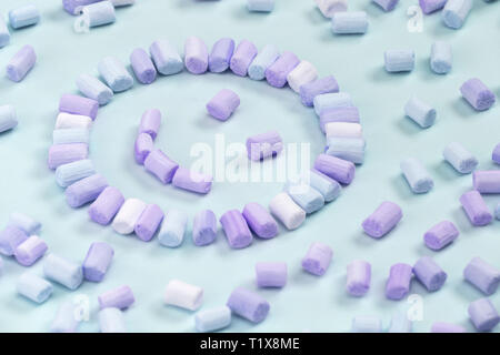 Top view of the multi-colored marshmallows which lies in the shape of a smiley or sun on a one-color pink background. Stock Photo
