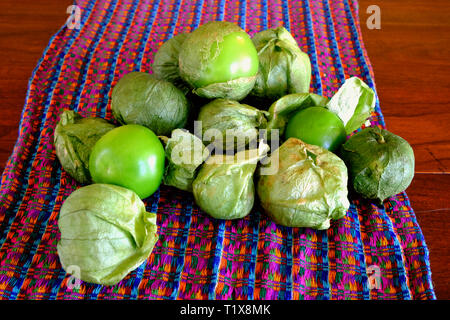 A pile of green tomatillos (Physalis philadelphica) on a colorfully patterned fabric; tomatillos with husks; peeled tomatillos. Stock Photo