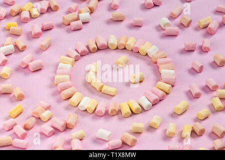 Top view of the multi-colored marshmallows which lies in the shape of a smiley or sun on a one-color pink background. Stock Photo