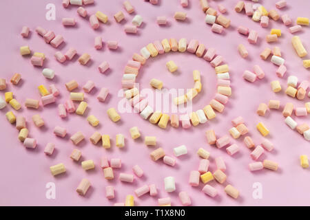 Top view of the multi-colored marshmallows which lies in the shape of a smiley or sun on a one-color pink background. Stock Photo