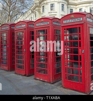 Four red traditional and heritage telephone boxes or kiosks stand in a row on the Strand, London, England, UK opposite Charing Cross Station. Stock Photo