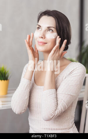Portrait Of Beautiful Young Woman with Natural Makeup applying white Under Eye Patches Beauty Mask On Face. Girl with eye patches. Woman with collagen Stock Photo