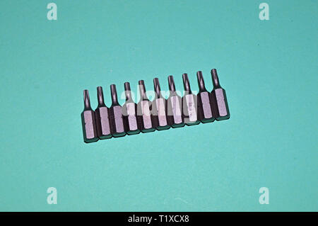 Various bits in a row in the bit holder. Bits for screwdrivers on the white surface. Cross bits. Flat-blade bits. Screw and unscrew fasteners Stock Photo