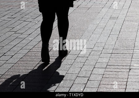 Silhouette of lonely woman walking down the street, black shadow on pavement. Female legs on the sidewalk, concept of loneliness, parting, diet Stock Photo