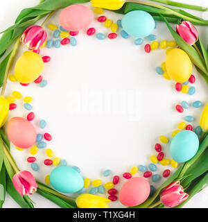 Easter wreath made of yellow tulips, colorful eggs and candies on white background. Flat lay. Stock Photo