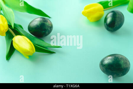 Spring concept with Easter eggs and yellow tulips on turquoise blue background. Copy space. Stock Photo