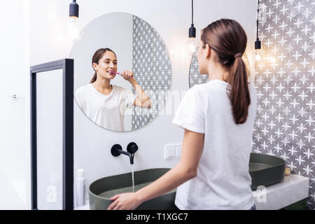 Appealing woman brushing teeth standing in the bathroom Stock Photo