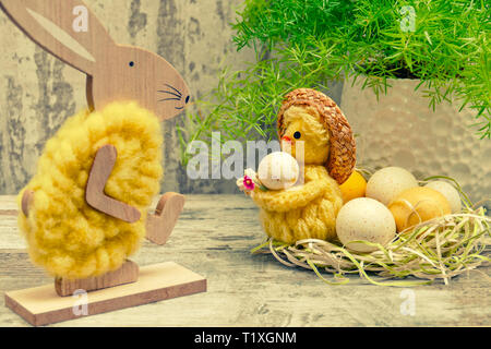 Easter concept with bunny walking towards chick in nest holding an egg, retro toned Stock Photo