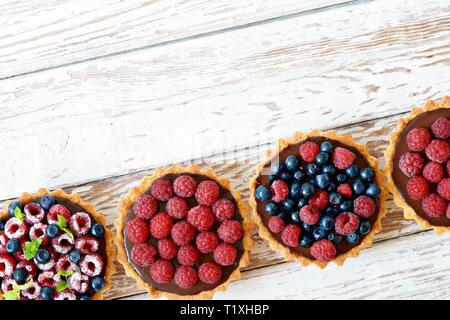 Raspberry and blueberry tartlets with chocolate ganache, fresh berries and mint leaves, selective focus. Fresh fruit tart on white background, freshly Stock Photo