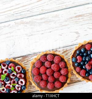 Raspberry and blueberry tartlets with chocolate ganache, fresh berries and mint leaves, selective focus. Fresh fruit tart on white background, freshly Stock Photo