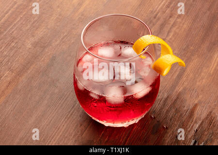 A photo of vibrant red cocktail with campari, an orange curl garnish, and ice cubes on a dark rustic wooden background with a place for text Stock Photo