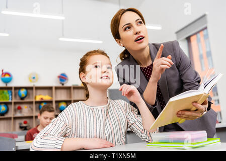 Teacher standing near desk and explaining lesson to pupil in classroom Stock Photo