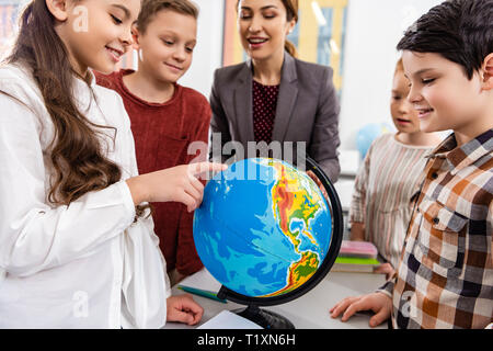 Teacher and pupils looking at globe while studying geography in classroom Stock Photo