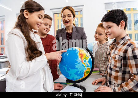 Teacher and pupils looking at globe while studying geography in classroom Stock Photo