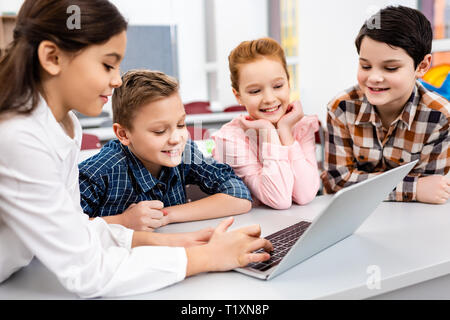 Happy preteen pupils using laptop in classroom with smile Stock Photo