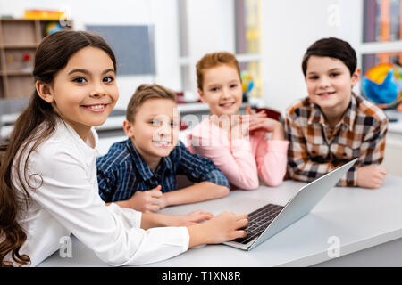 Happy preteen pupils using laptop in classroom with smile Stock Photo