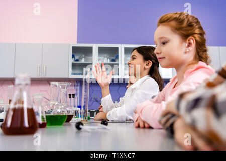 Smiling schoolgirl raising hand in class during chemistry lesson Stock Photo