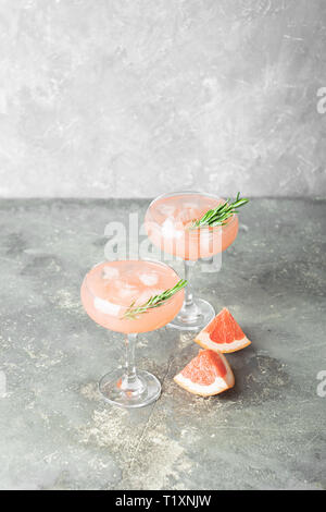 Refreshing summer cocktail of grapefruit juice of rosemary and ice in two glass glasses on gray background of concrete. Stock Photo