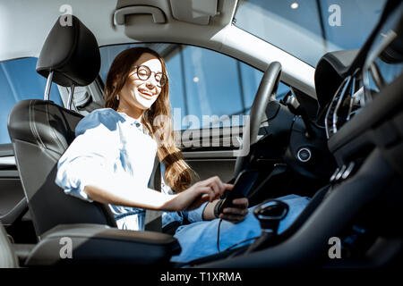 Young and cheerful woman using smart phone while sitting in the modern car in the city Stock Photo