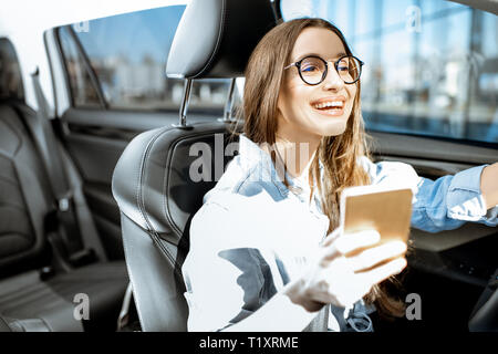 Young and cheerful woman using smart phone while driving a modern car in the city Stock Photo