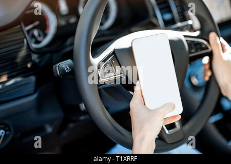 Woman holding a smart phone with empty screen to copy paste while driving a car on the steering wheel Stock Photo