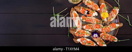 Salmon sandwiches with cream cheese and microgreen on wooden table. Canape with salmon. Banner.  Top view Stock Photo