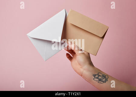 partial view of woman with tattoo holding white and beige envelopes on pink background Stock Photo