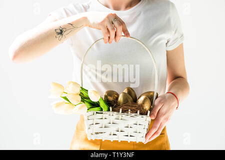 partial view of woman holding white straw basket with Easter eggs and tulips isolated on white Stock Photo