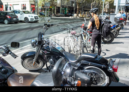 Girl commuter parks her bicycle beside motorbikes on the pavement in Melbourne city centre,Victoria,Australia Stock Photo