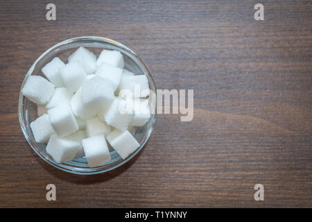 Top view of sugar cubes in a glass bowl on a wooden background. Copy space provided. Stock Photo